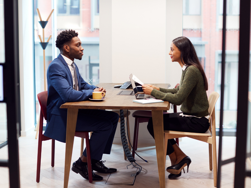 A man and a woman faceing each other while seated at a table, the woman has notes while she interviews the man for the property manager position.